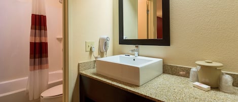 A bathroom with a white sink, a mirror, a shower curtain, and a toilet.