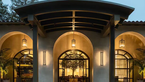 A building with three arched entryways, each with a hanging light fixture and a view of an interior space.