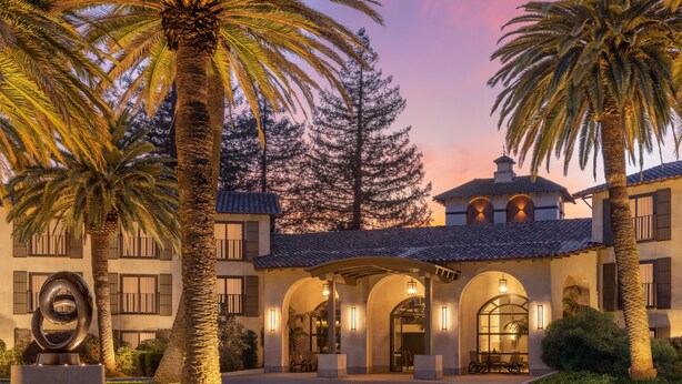 A building with a courtyard, palm trees, and a sculpture.