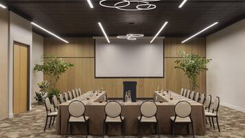Un salón de conferencias con una larga mesa, sillas, una pantalla de proyector y un moderno candelabro.