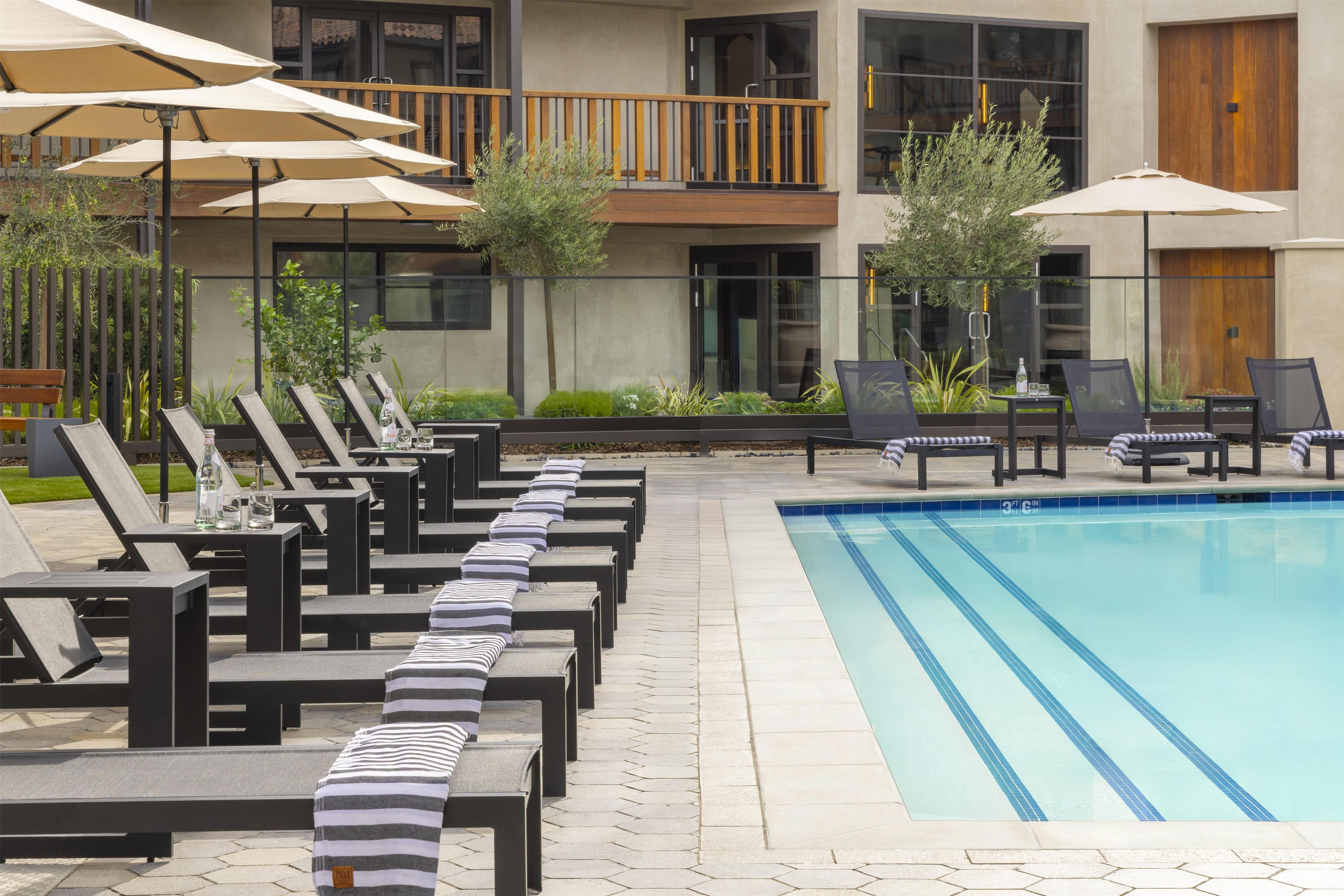 A poolside area with lounge chairs, umbrellas, and a swimming pool.