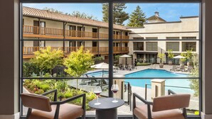A view from a balcony with a pool, outdoor seating, and a building with balconies.