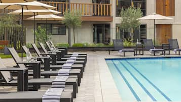 Una piscina al aire libre, sombrillas, sillones reclinables de piscina