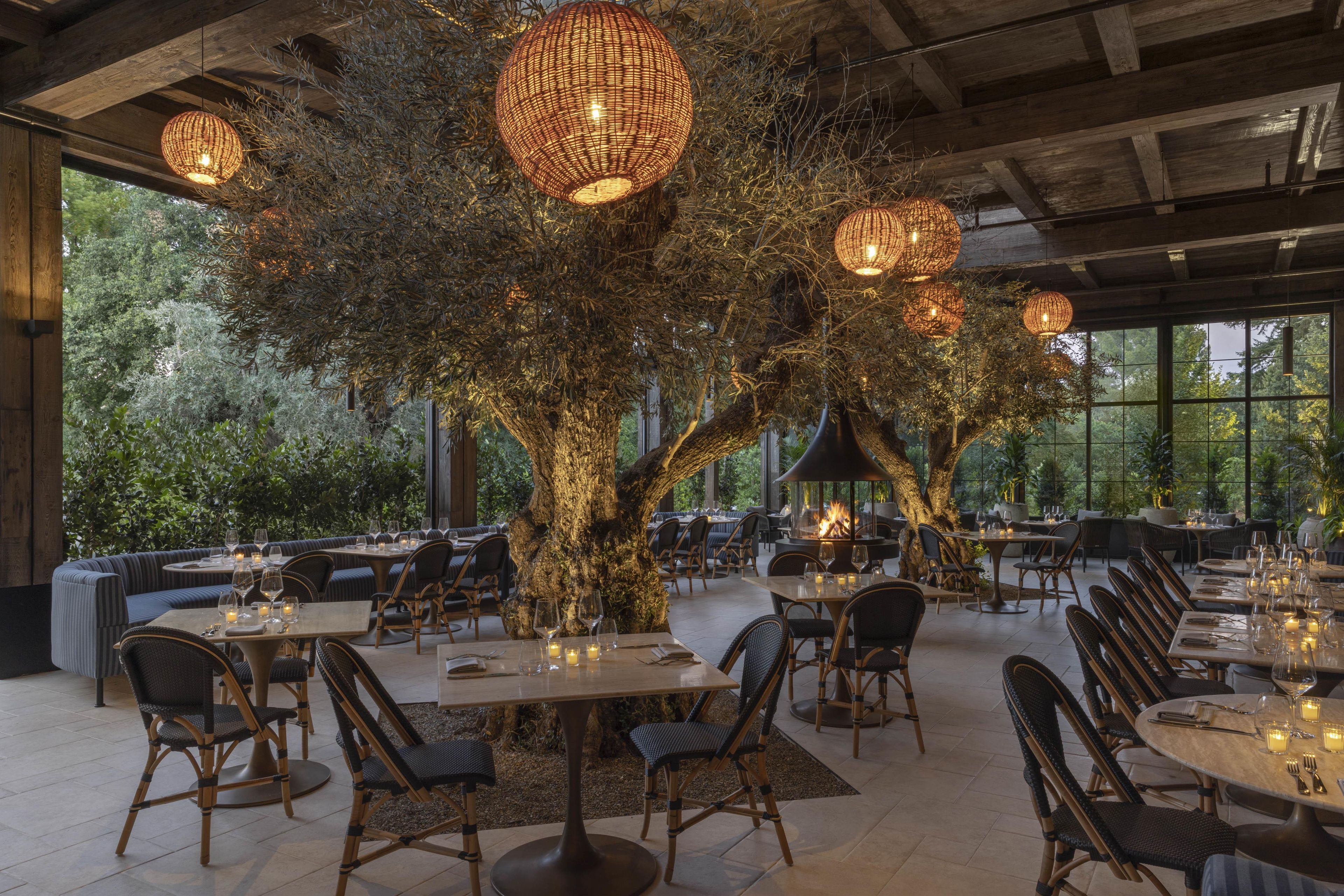 A restaurant with round tables, wicker chairs, and hanging lights.