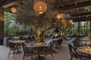 A restaurant with round tables, wicker chairs, and hanging lights. - Casa Mani Resort Napa Valley, Curio Collection by Hilton (Napa)