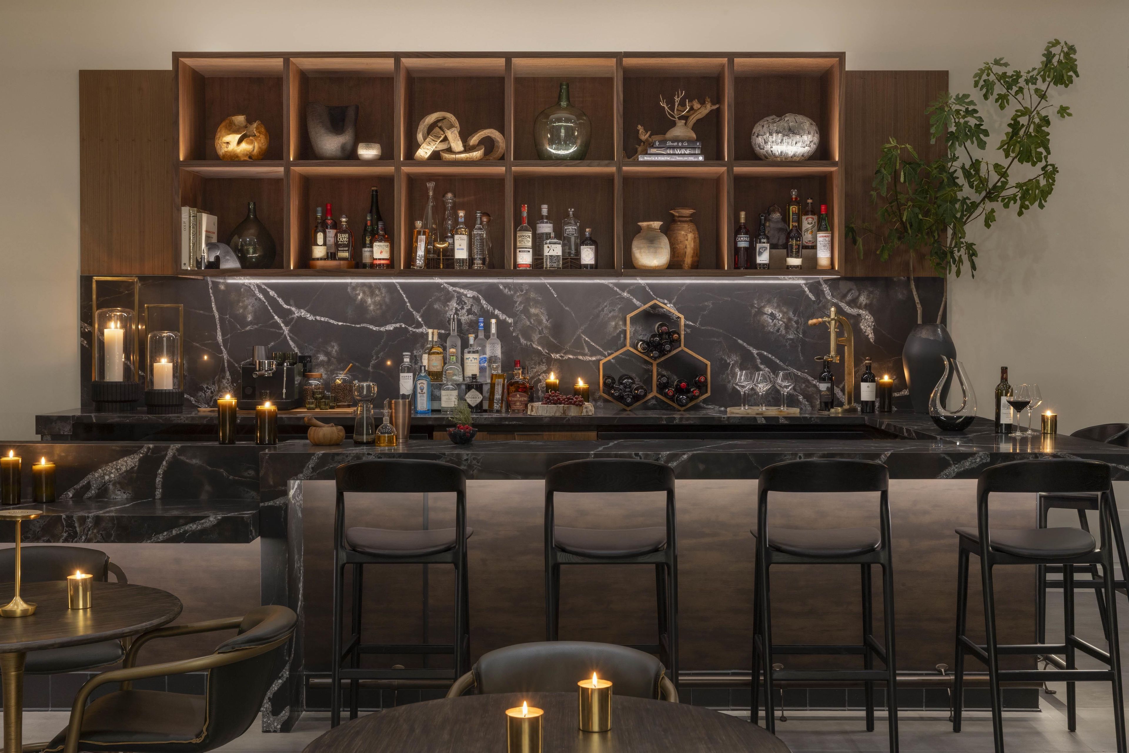 Een bar met een marmeren aanrecht, flessenplanken en zitplaatsen met kaarsen.