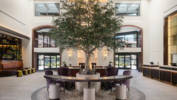 A spacious lobby with a central tree, seating area, and a reception desk.