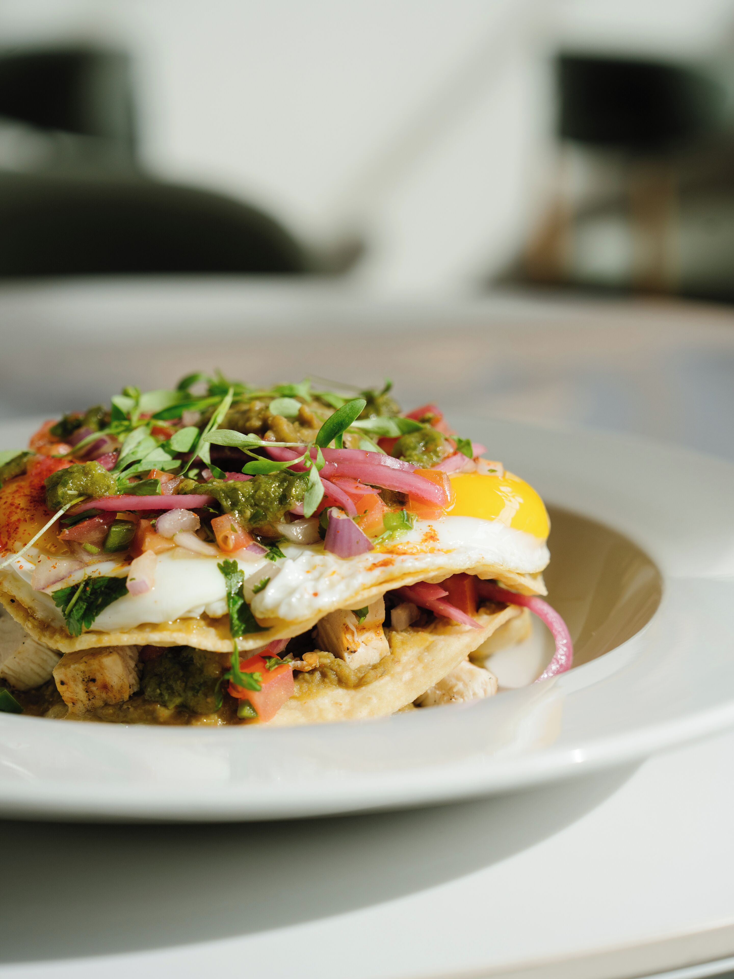 A plate with a layered dish, including a fried egg, greens, and red onions.