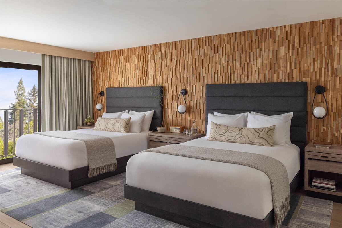 Ein Hotelzimmer mit zwei Betten, einer Holzwand, einem Balkon und Blick auf Bäume.