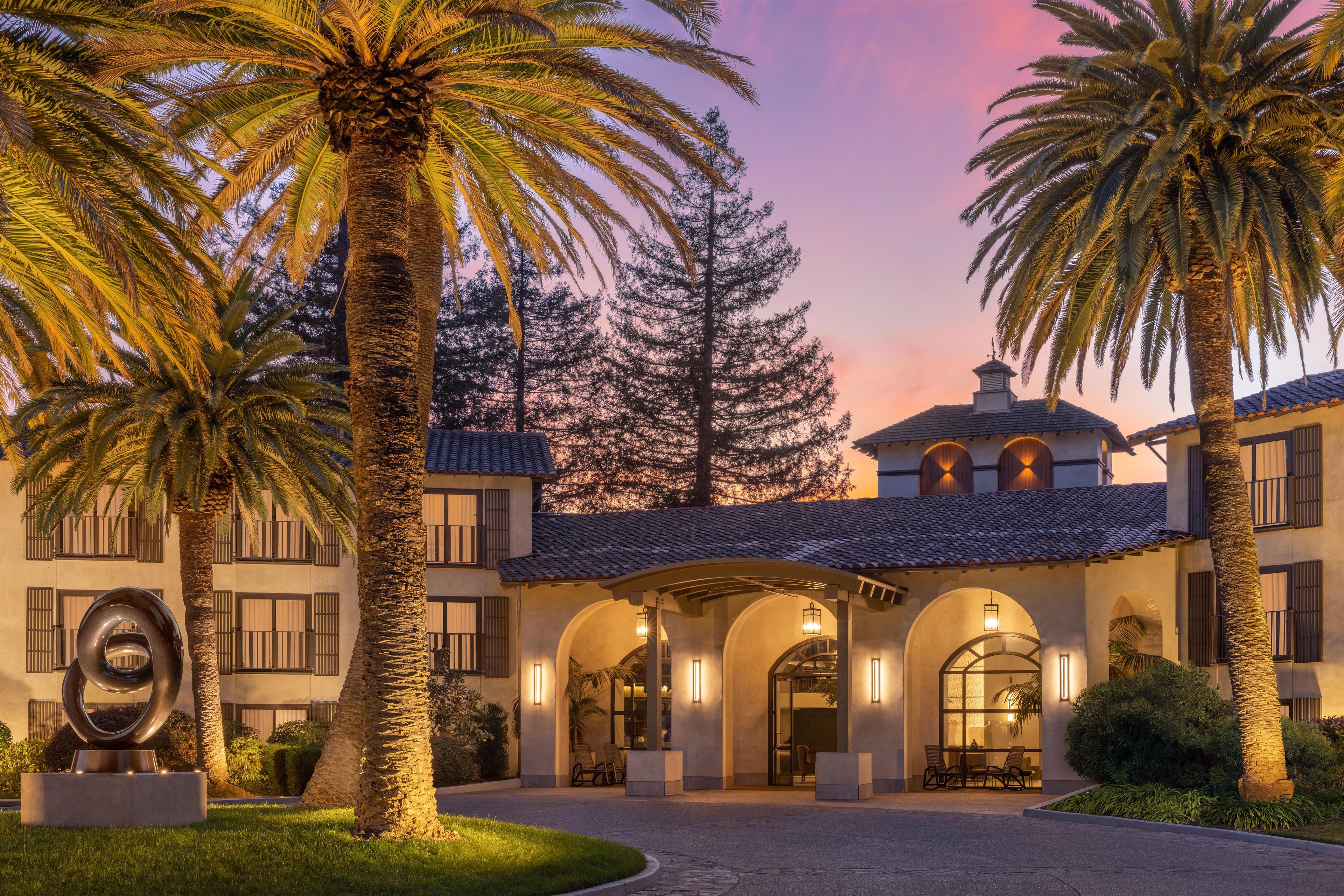 A building with a courtyard, palm trees, and a sculpture.