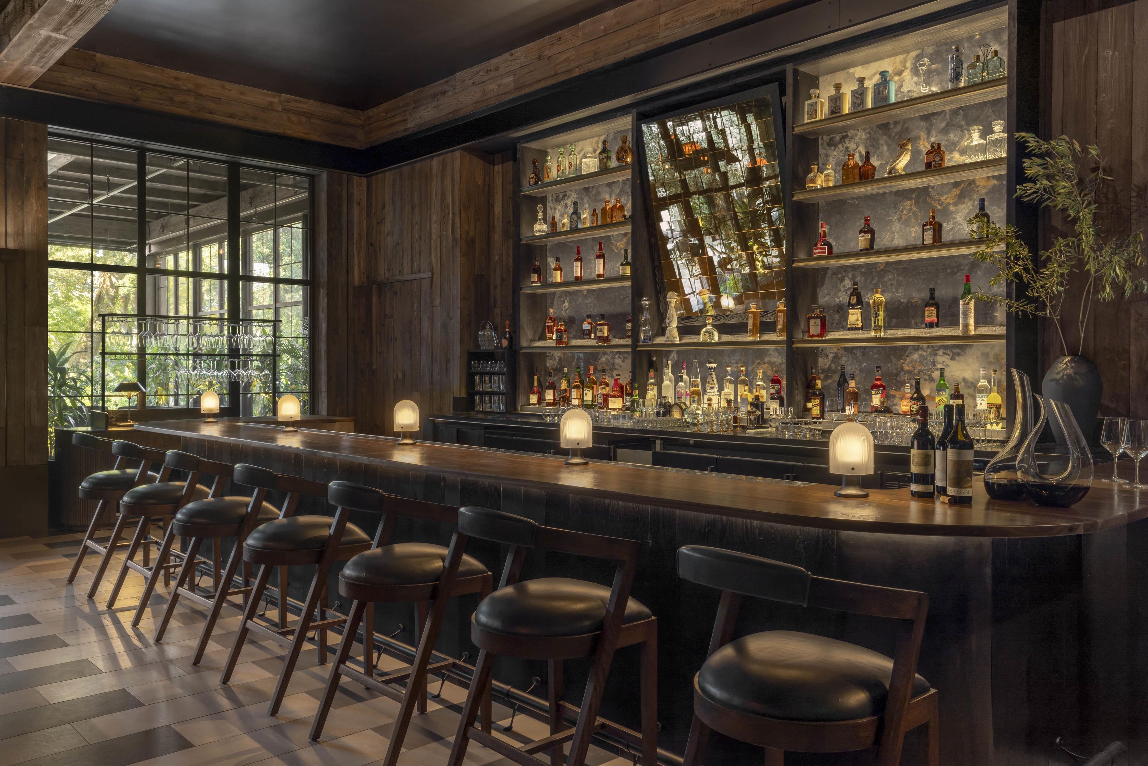 A bar with a long counter, multiple shelves of bottles, and bar stools.