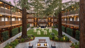 A hotel courtyard with outdoor seating, large trees, and a central hexagonal structure.