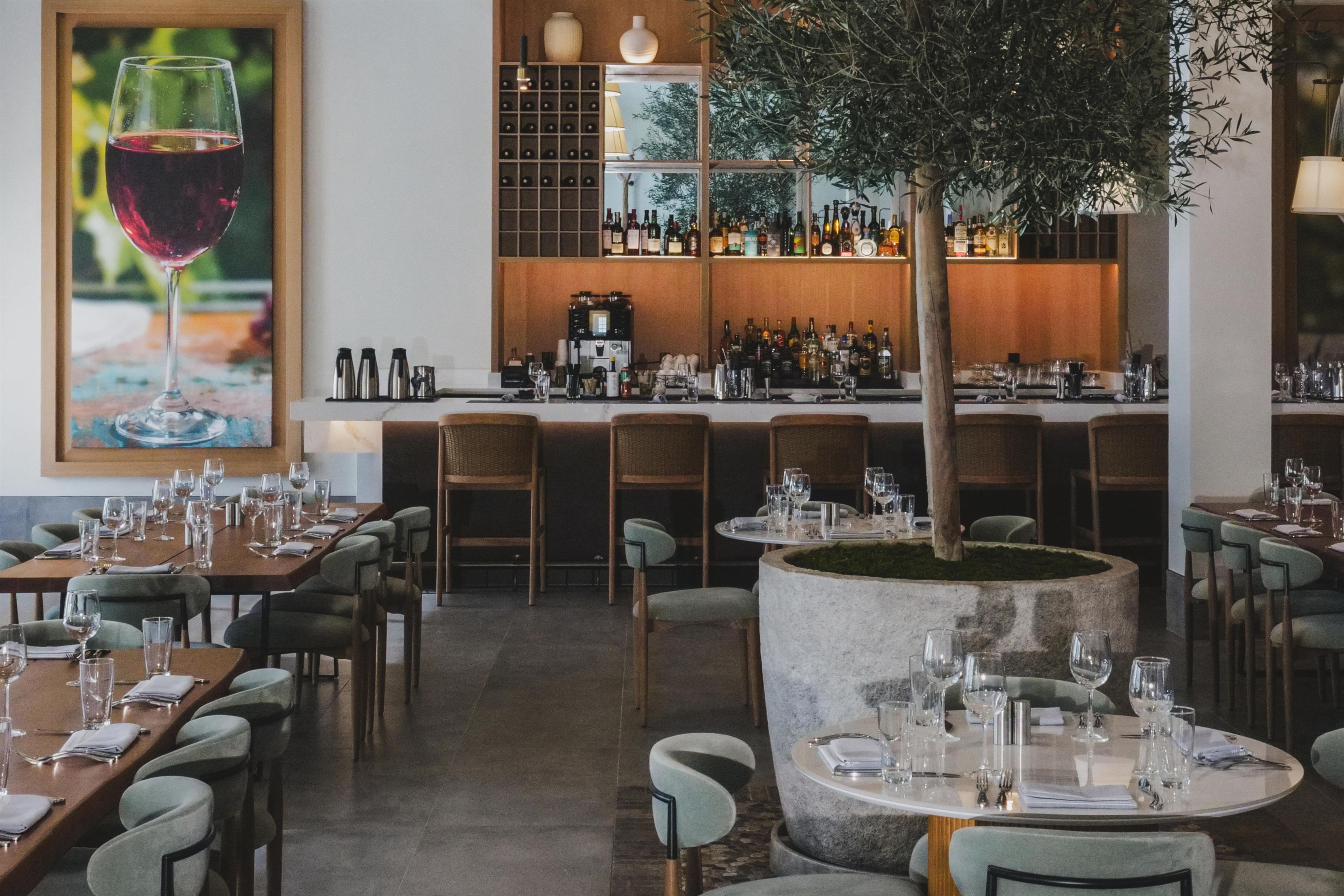 A restaurant with multiple dining tables, chairs, and a bar area with shelves of bottles.