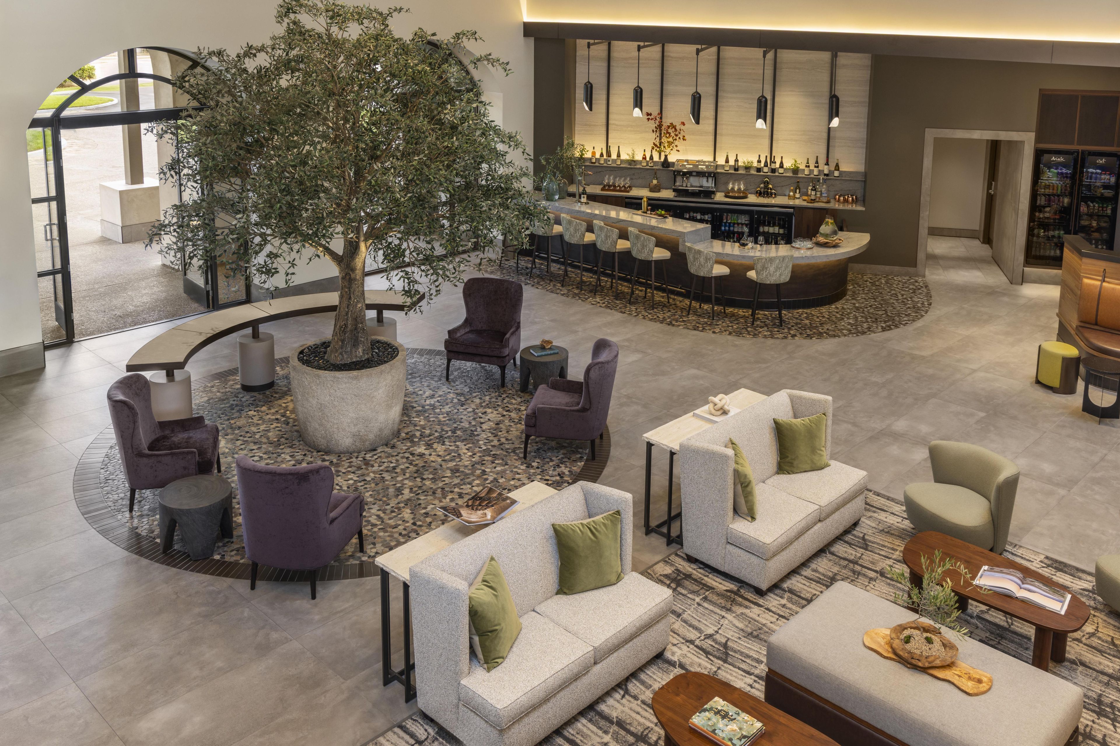 Eine Hotlelloge mit einer zentralen Sitzecke, einer Bar und einem großen Baum.