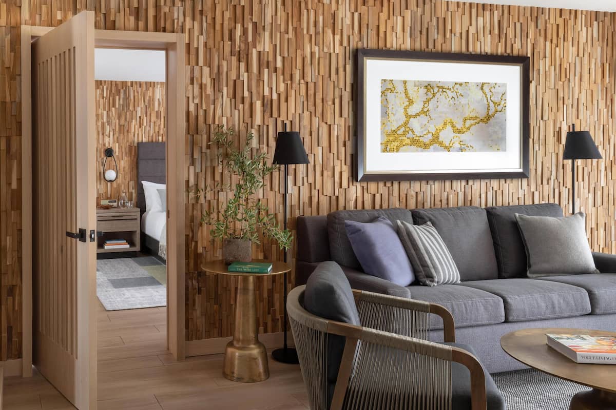 Ein modernes Wohnzimmer mit einer Holzvertäfelung, einem grauen Sofa, einem kleinen runden Tisch, einer Topfpflanze und einem gerahmten Kunstwerk.