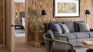 A modern living room with a wooden wall panel, a grey sofa, a small round table, a potted plant, and a framed artwork.