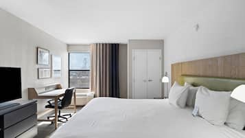 Habitación de hotel con cama, escritorio, silla, televisor y vista a la ciudad.