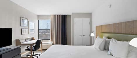 Habitación de hotel con cama, escritorio, silla, televisor y vista a la ciudad.