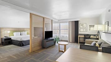 A hotel room with a bed, a desk, a TV, a dining table, and a sofa.