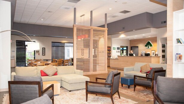 Un moderno vestíbulo de hotel con mostrador de recepción, zona de estar con sofás y sillones, y una mampara decorativa de madera.