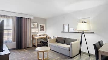 Een hotelkamer met een bureau, een bank, een kleine tafel, een lamp en ingelijste foto's aan de muur.