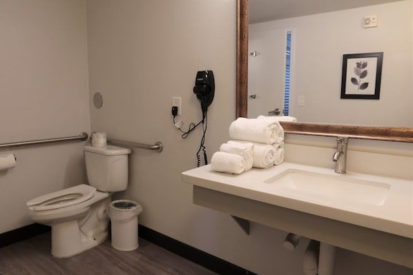 Un baño con inodoro, secador de manos, lavamanos y espejo.