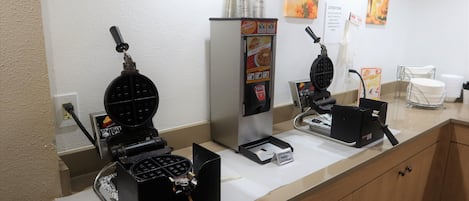 A kitchen area with waffle makers, a refrigerator, and a coffee machine.