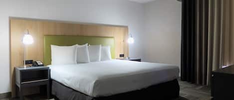 A hotel room with a large bed, two bedside tables with lamps, a wooden headboard, and a dark curtain on the window.