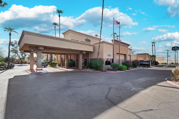 A hotel with a covered entrance, palm trees, and an American flag.