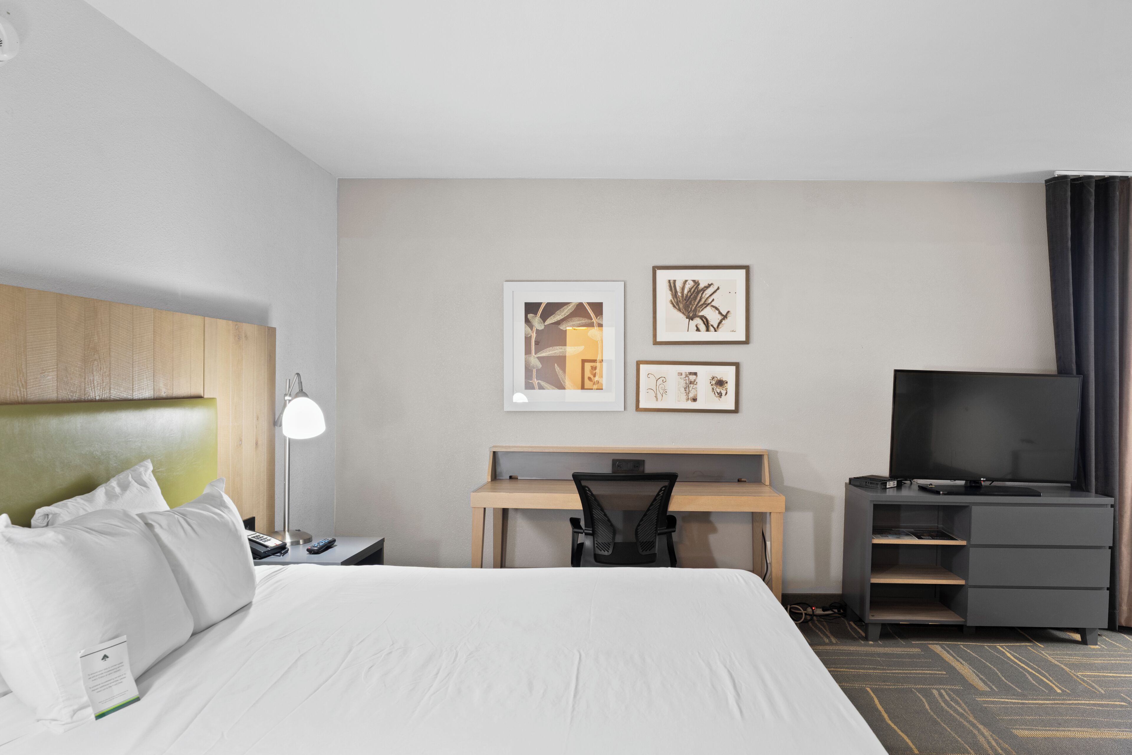 Une chambre d’hôtel équipée d’un lit, d’un bureau, d’une chaise, d’une télévision et d’œuvres d’art accrochées au mur.