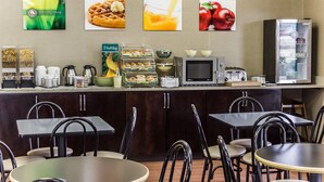 A breakfast bar with various food items, a microwave, and a refrigerator. There are chairs and tables arranged around the bar.
