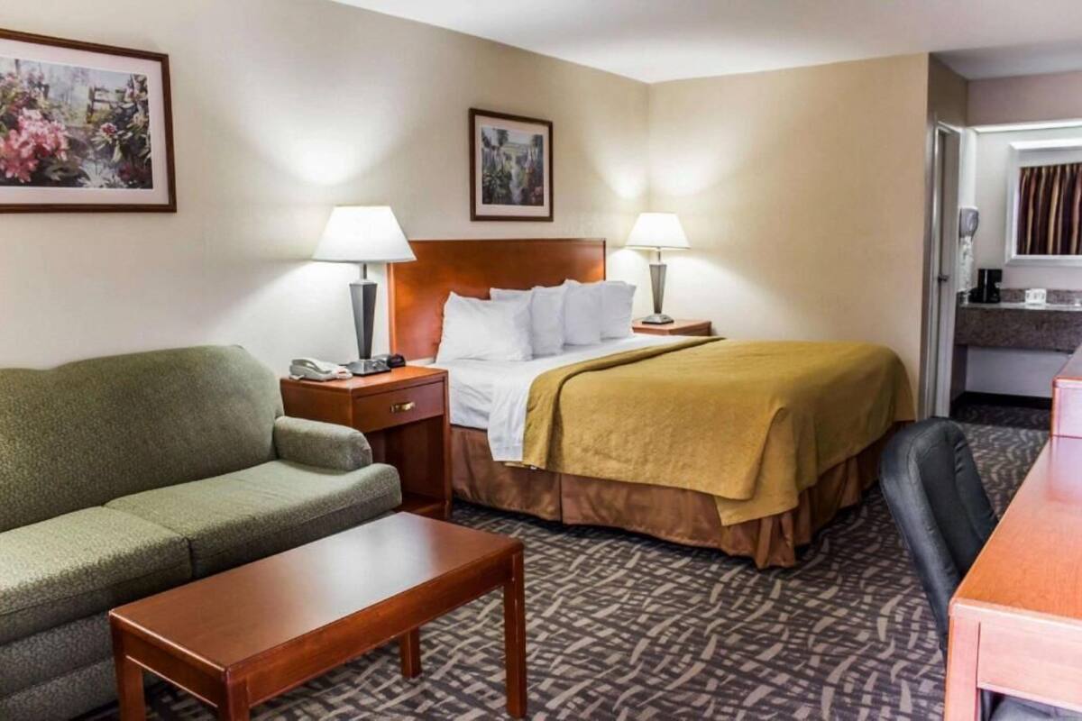 A hotel room with a bed, two bedside tables, a sofa, a coffee table, and a desk.