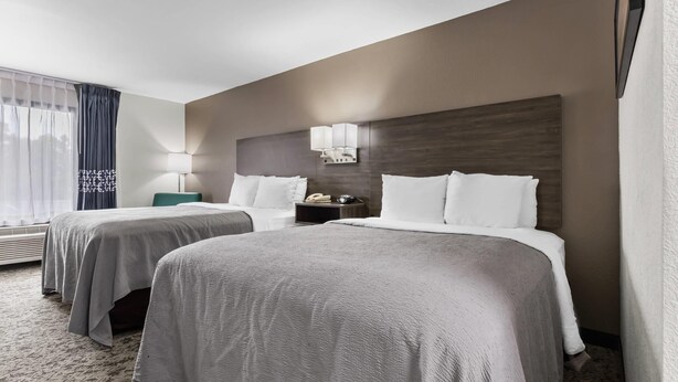 A hotel room with two beds, a nightstand, a lamp, and a window with curtains.