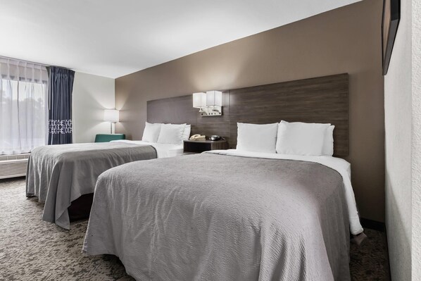 A hotel room with two beds, a nightstand, a lamp, and a window with curtains.