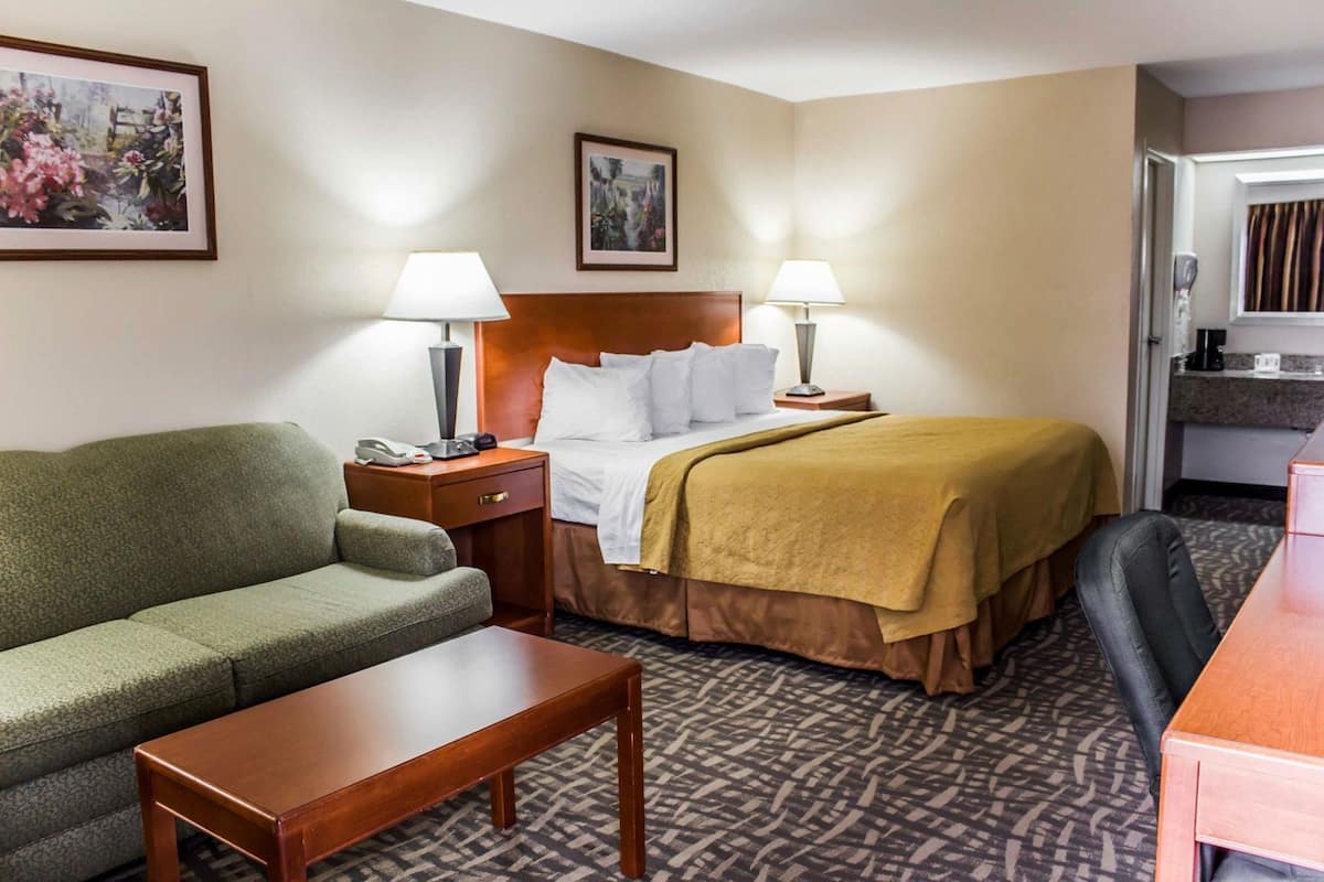 A hotel room with a bed, a sofa, a desk, two lamps, a telephone, and a painting on the wall.