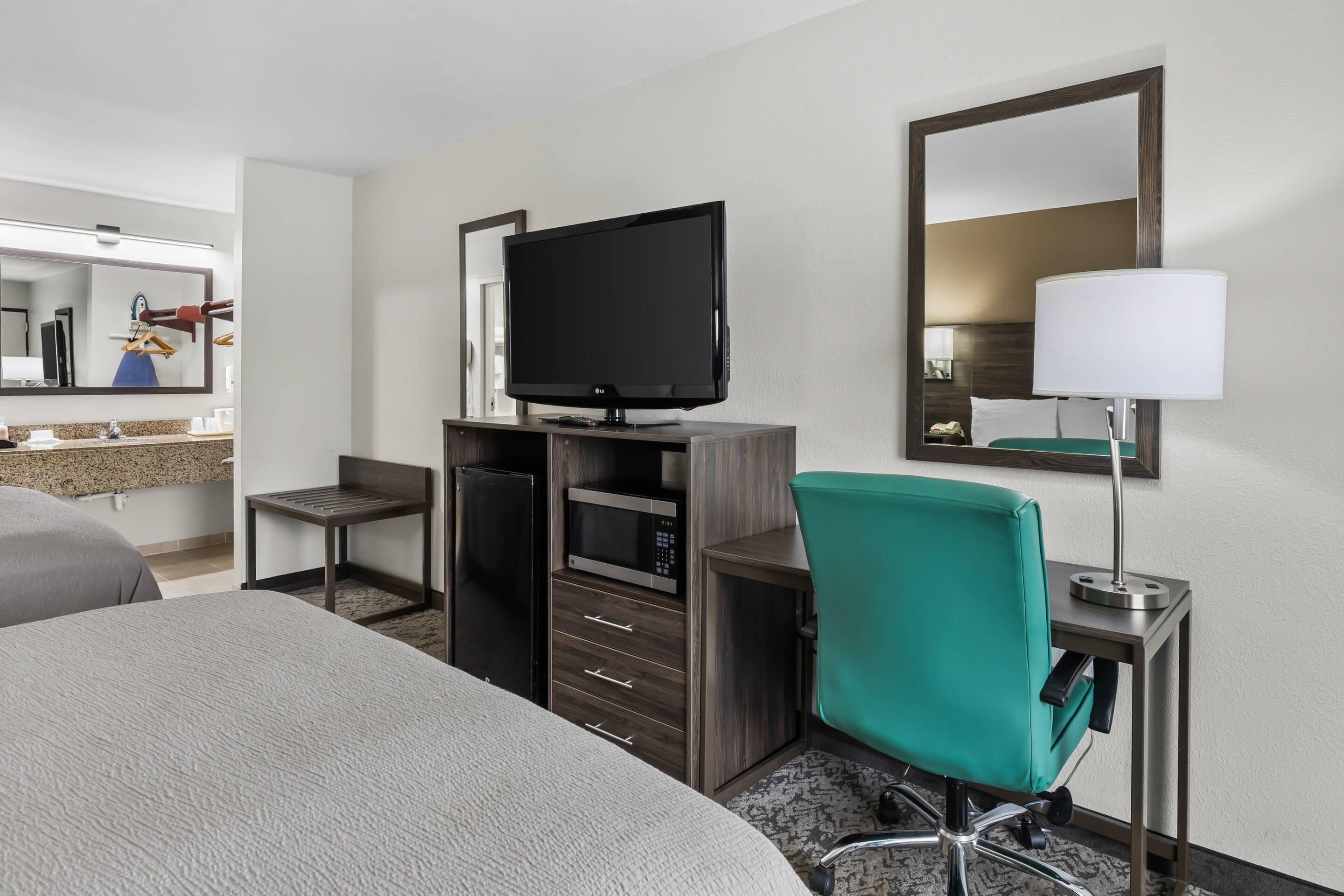 Een hotelkamer met een bed, een bureau met een flatscreen televisie, een stoel, een bureaulamp en een spiegel.