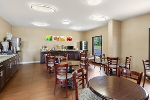 Un comedor con mesas y sillas de madera, una cocina con electrodomésticos, y vista a zonas verdes.
