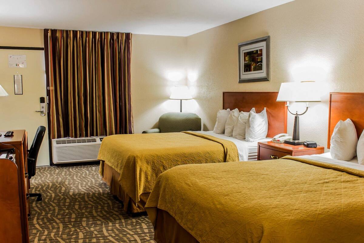 A hotel room with two beds, a desk, a chair, a lamp, and a picture on the wall.