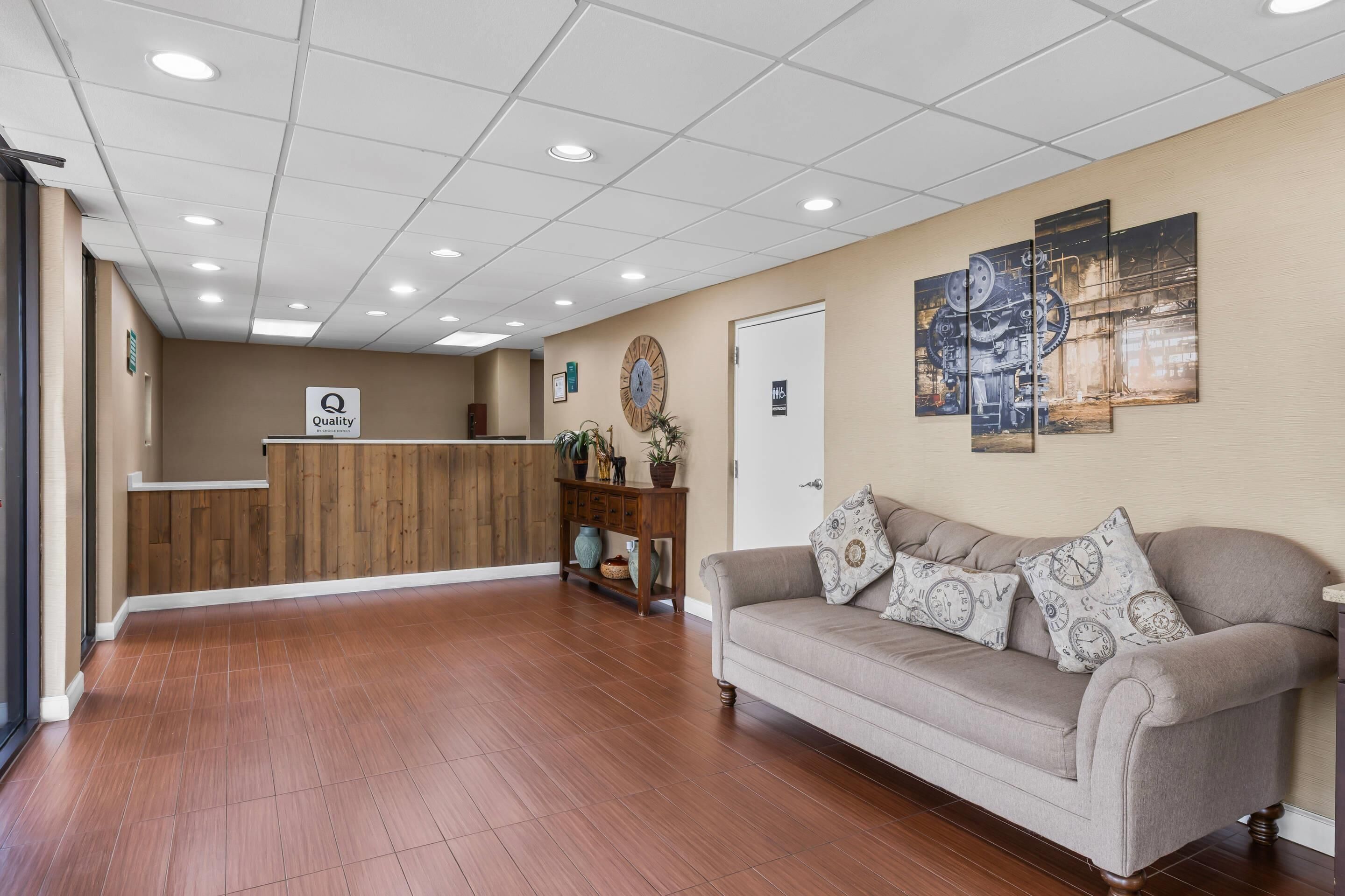 A hotel reception area with a wooden reception desk, a couch with patterned cushions, and a wall clock.
