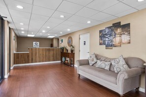 A hotel reception area with a wooden reception desk, a couch with patterned cushions, and a wall clock. - Quality Inn Kinston Hwy 70 (Kinston)