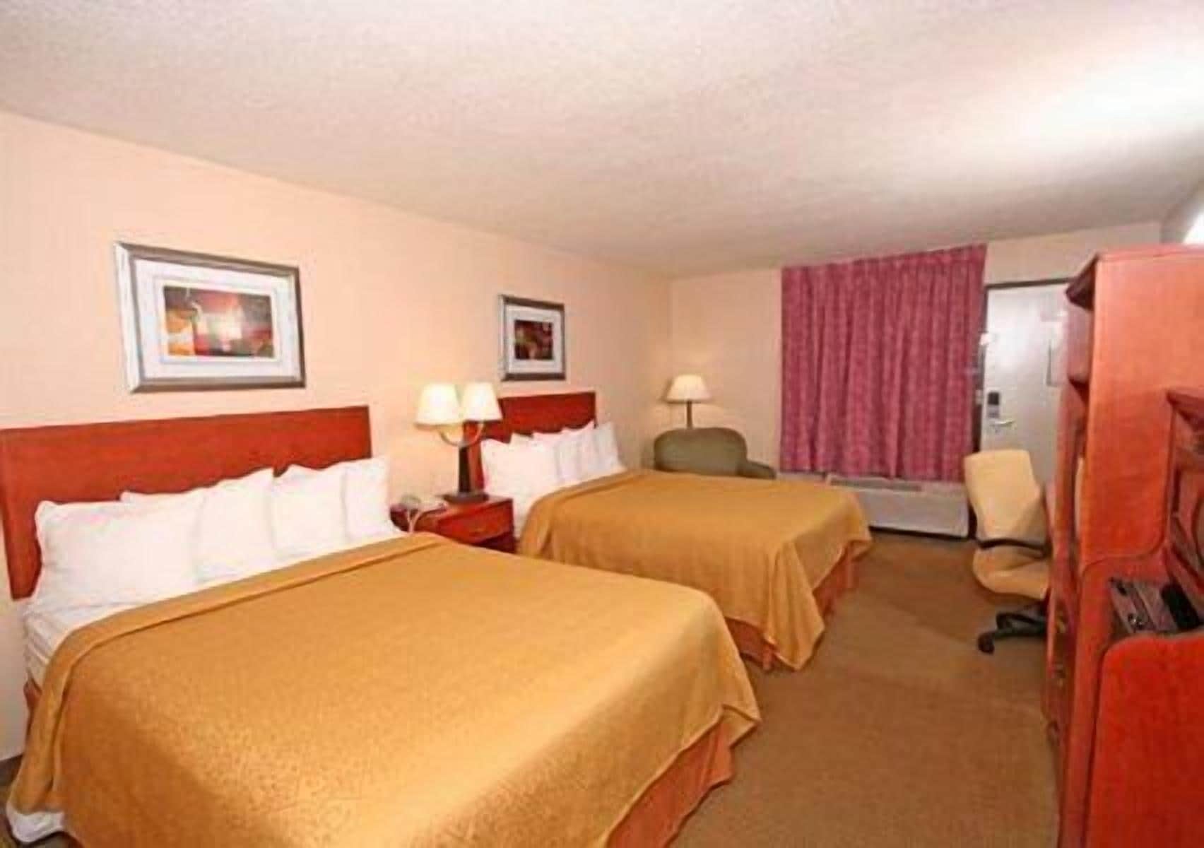 A hotel room with two beds, a desk, a chair, and a window with curtains.