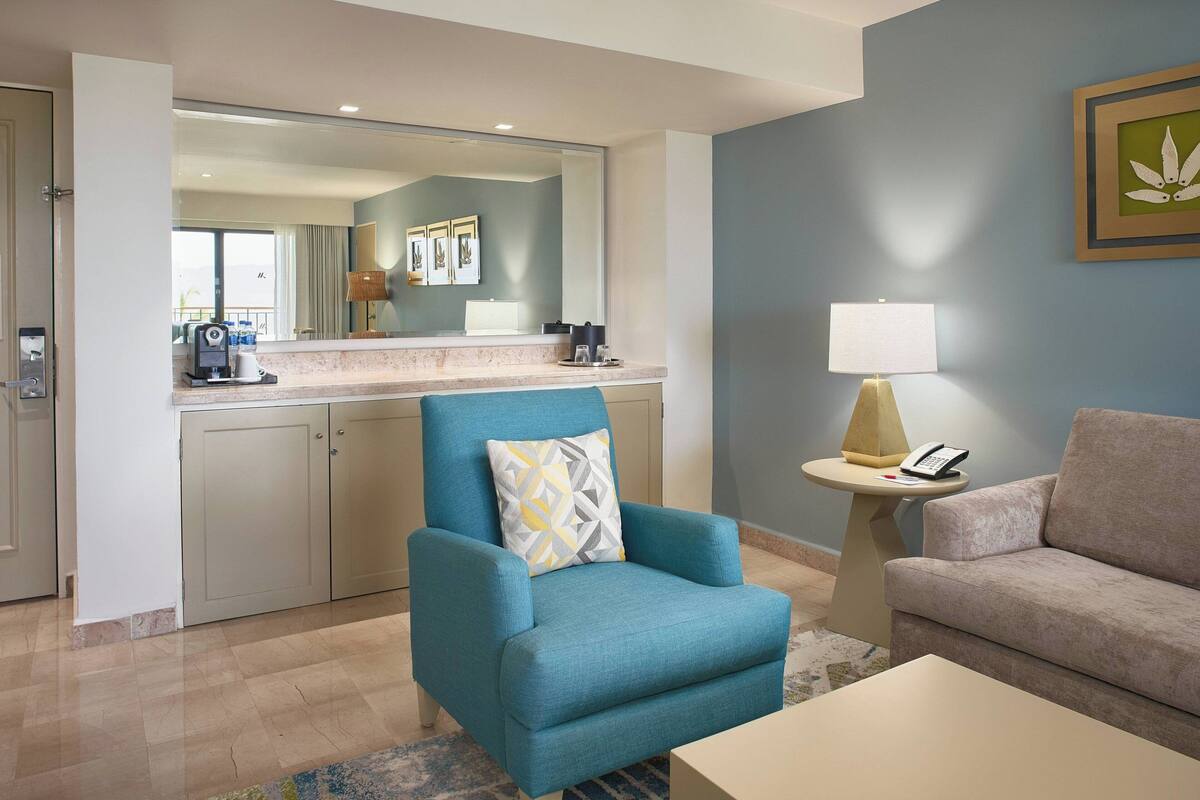 A modern living room with a blue armchair, beige sofa, and a coffee station.