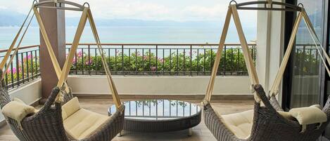 Two wicker swing chairs with cushions on a balcony with a view of the sea.