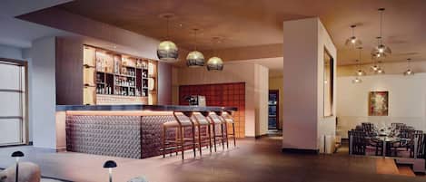 Un área de bar moderna con mostrador, taburetes y lámparas colgantes.