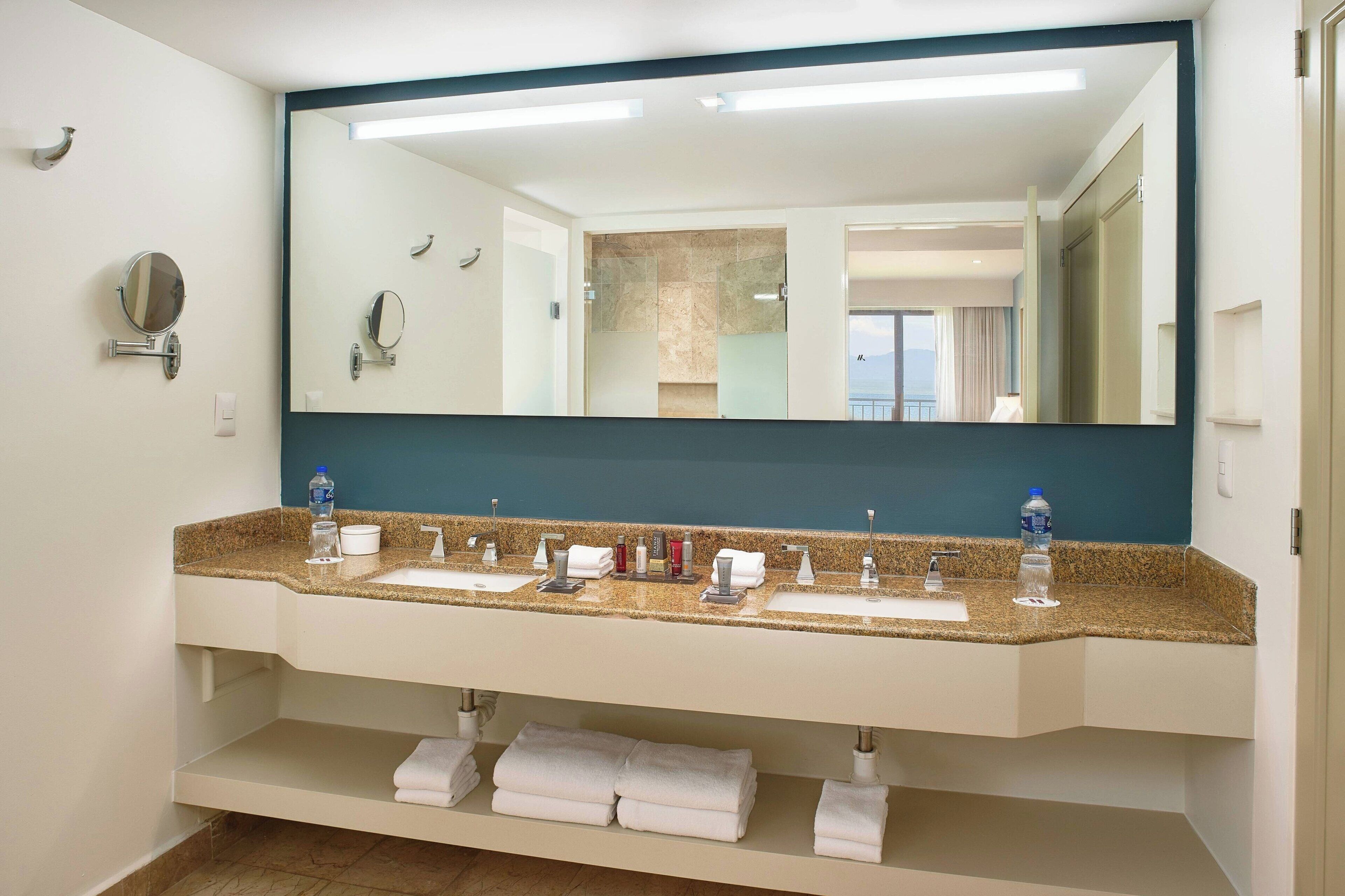 A hotel bathroom with a large mirror, two sinks, and a towel rack.