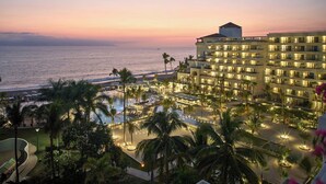 Ein Resort mit Pool, Palmen und Blick auf den Ozean bei Sonnenuntergang.
