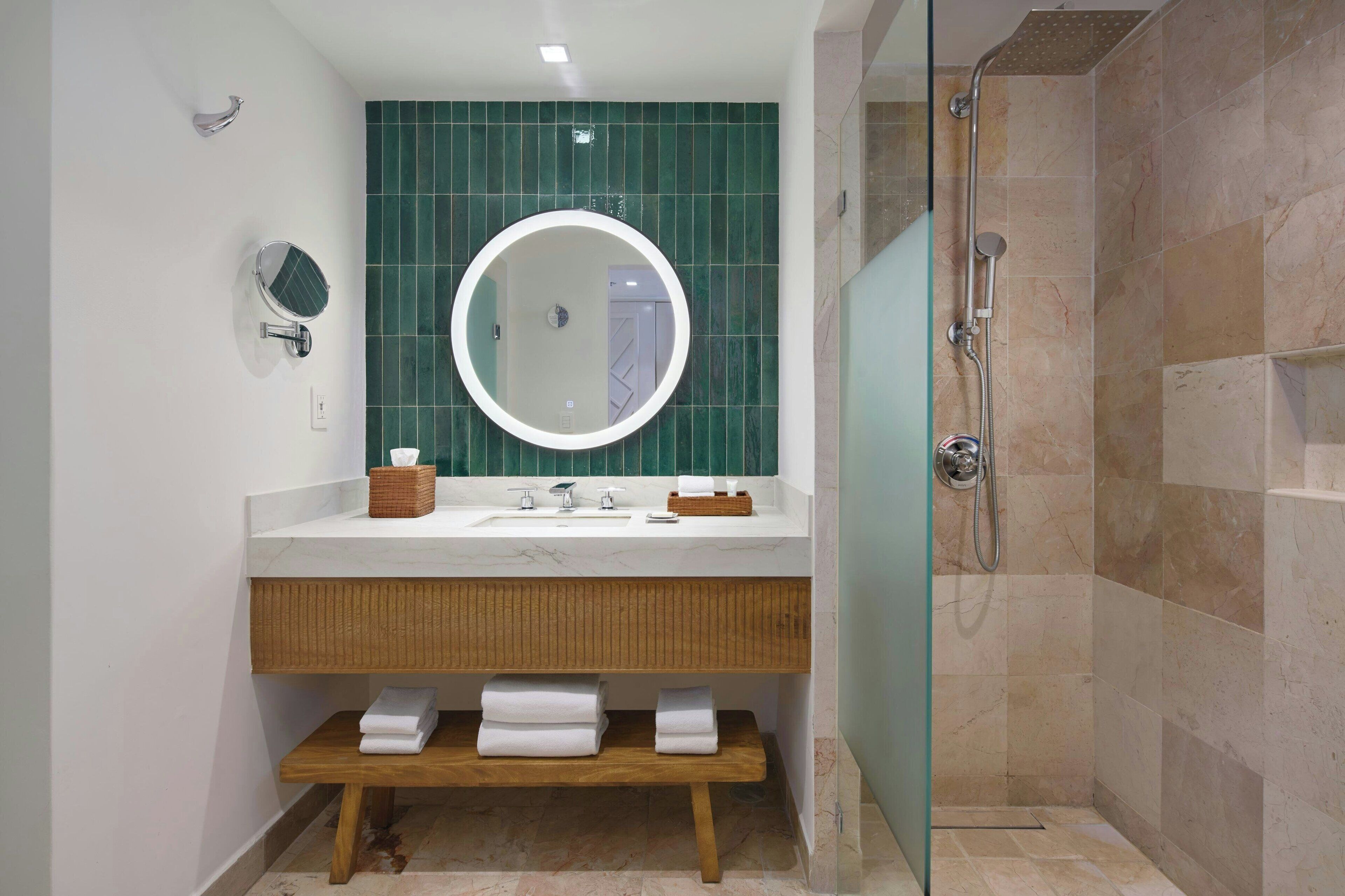 A modern bathroom with a white sink, mirror, and green-tiled wall.