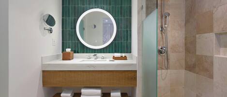 A modern bathroom with a white sink, mirror, and green-tiled wall.