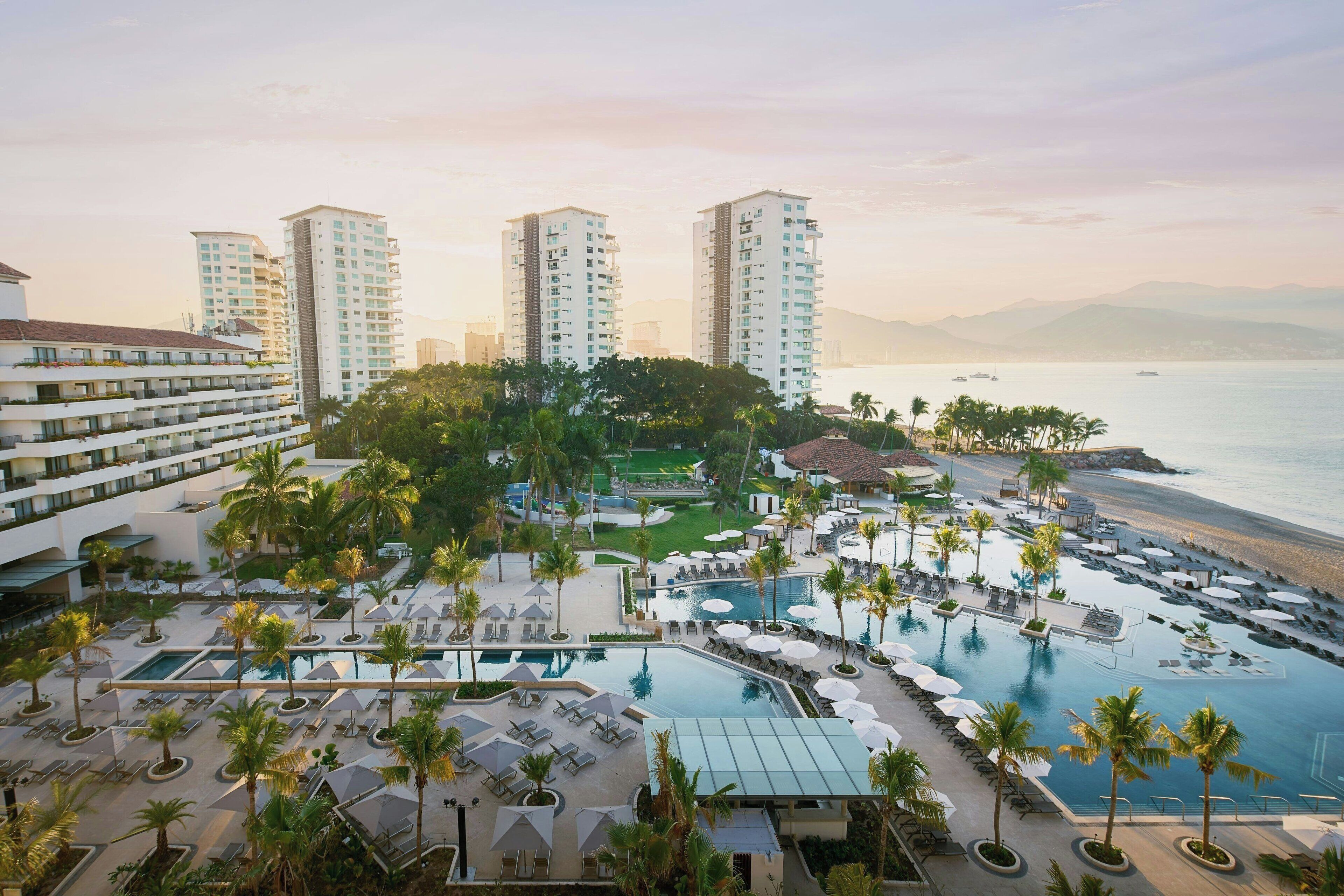 Un complexe hôtelier doté de plusieurs piscines, de palmiers et offrant une vue sur la plage.