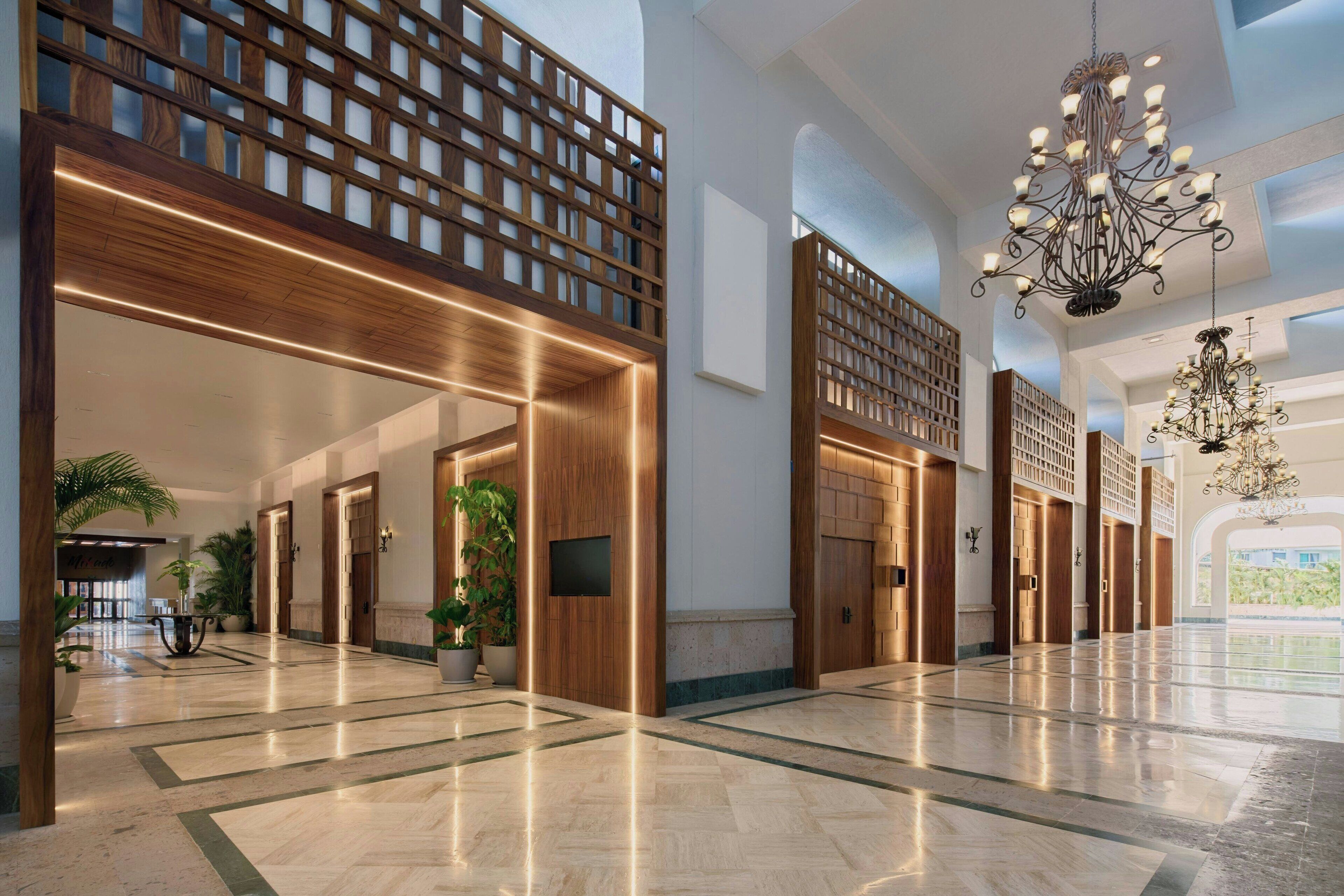 Un hall d’entrée spacieux, agrémenté de boiseries, d’un grand lustre et de plantes en pot.